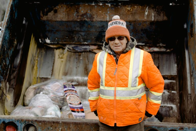 Garbage man in uniform near truck with rubbish